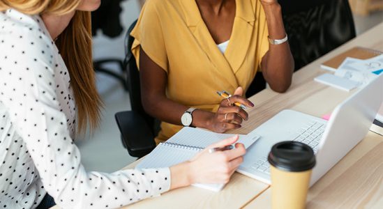Two women discussing in table with their notebooks