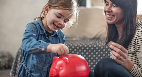 Daughter putting coin in piggy bank while mom is looking at her