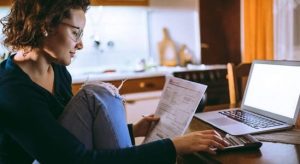 Woman using laptop and looking at her paper