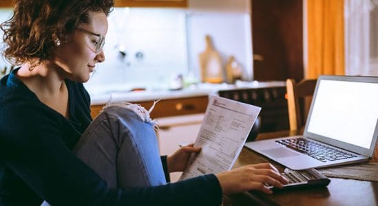 Woman using laptop and looking at her paper