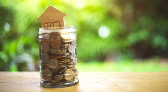 Coins with toy model house sitting on top