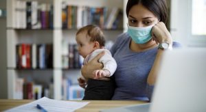 Woman holding a baby while looking a her laptop