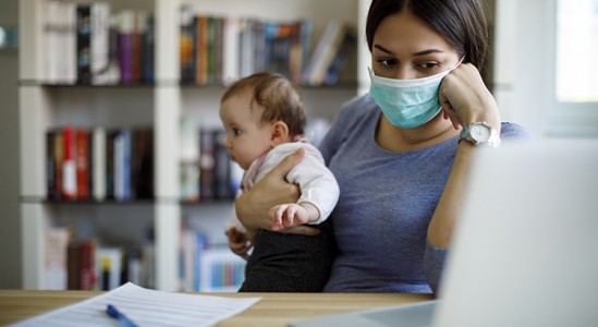 Woman holding a baby while looking a her laptop