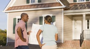 Couple holding a blueprint while standing in front of a house