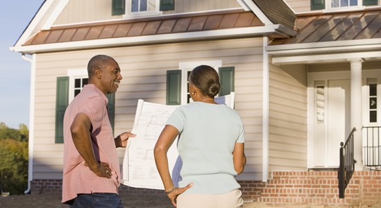 Couple holding a blueprint while standing in front of a house