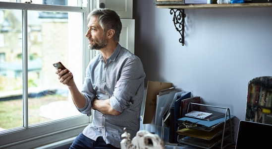 Man looking outside the window while holding his phone