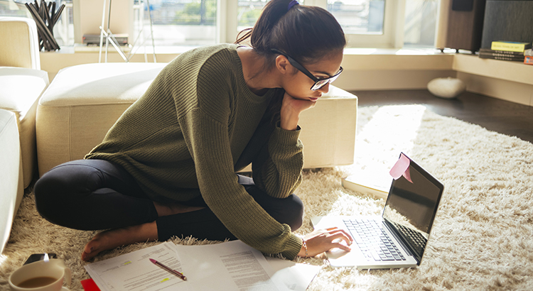 young woman studying and working on her laptop,sitting on the carpet in the living room, nice sunny day
