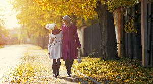 Happy mother and daughter walking in the street in the autumn. The girl is aged 9 and the mother is in her 30s. They are wearing coats, scarfs and caps.