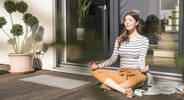 Young woman sitting on terrace at home practicing yoga