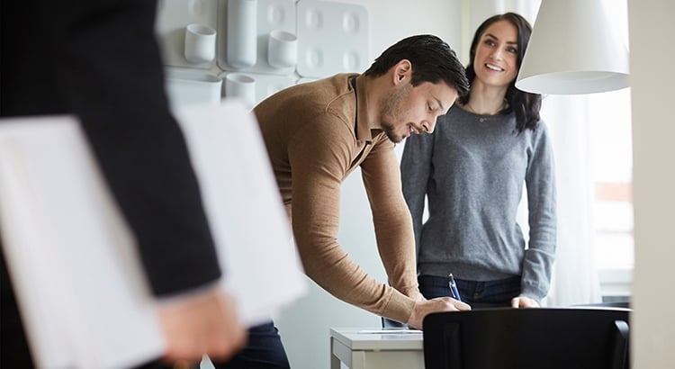Woman looking at real estate agent while man signing documents at new home