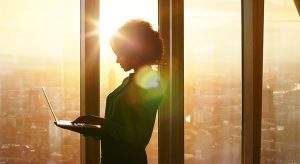 Businesswoman on laptop at window in morning sun