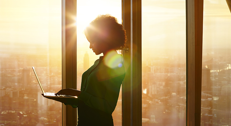 Businesswoman on laptop at window in morning sun