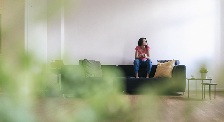 Woman at home sitting on sofa with cup of coffee