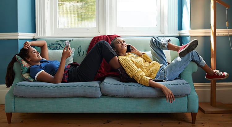 Smiling friends using phone while lying on sofa