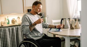 Tattooed mature man reading mail while holding coffee cup on wheelchair at home