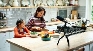 Woman vlogging at home with video camera on worktop and daughter's watching