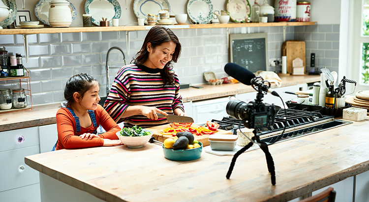 Woman vlogging at home with video camera on worktop and daughter's watching