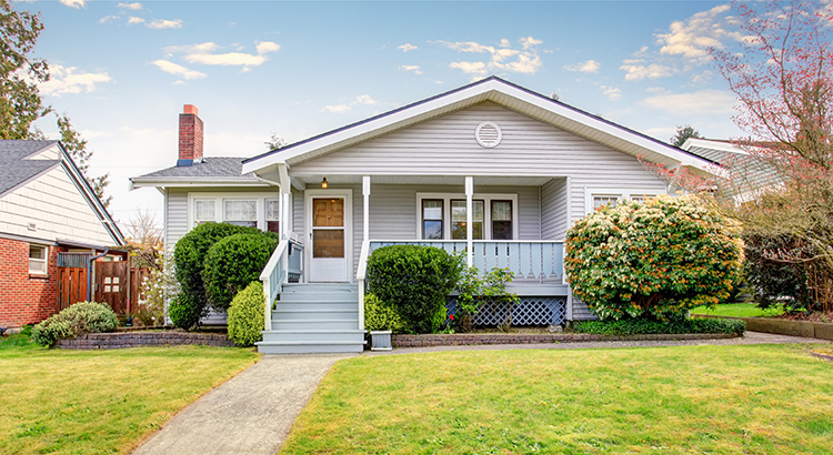 Beige siding house exterior with covered porch and trimmed bushes in front. View of soft blue staircase with narrow walkway.