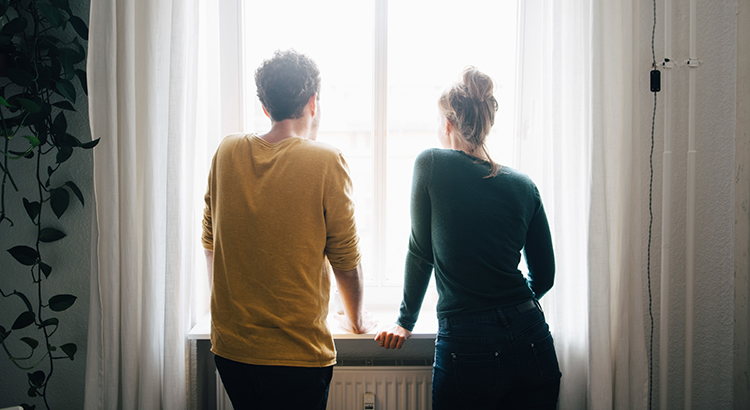 Rear view of couple looking through window while standing at home