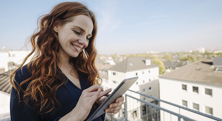 Smiling redheaded woman using tablet on rooftop terrace