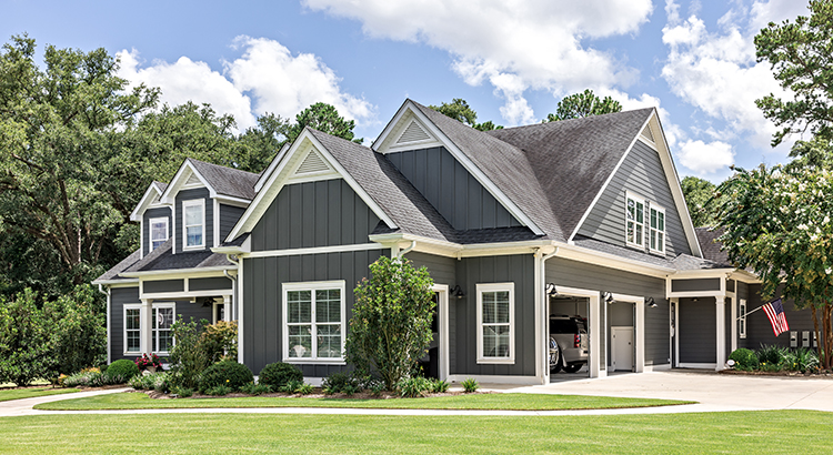 A large gray craftsman new construction house with a landscaped yard and leading pathway sidewalk