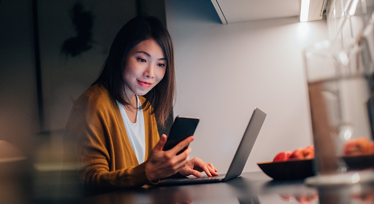 Young Woman Using Smartphone While Working With Laptop At Home In The Dark