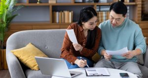 Couple reviewing household bills and paperwork together, with a laptop on the coffee table.